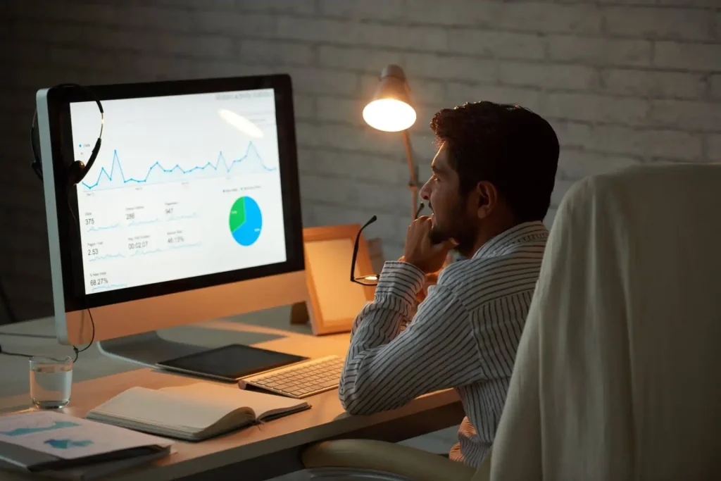 Homem analisando gráfico de campanha em plataforma de campanha de incentivo em ambiente de escritório com laptop e gráficos na tela.